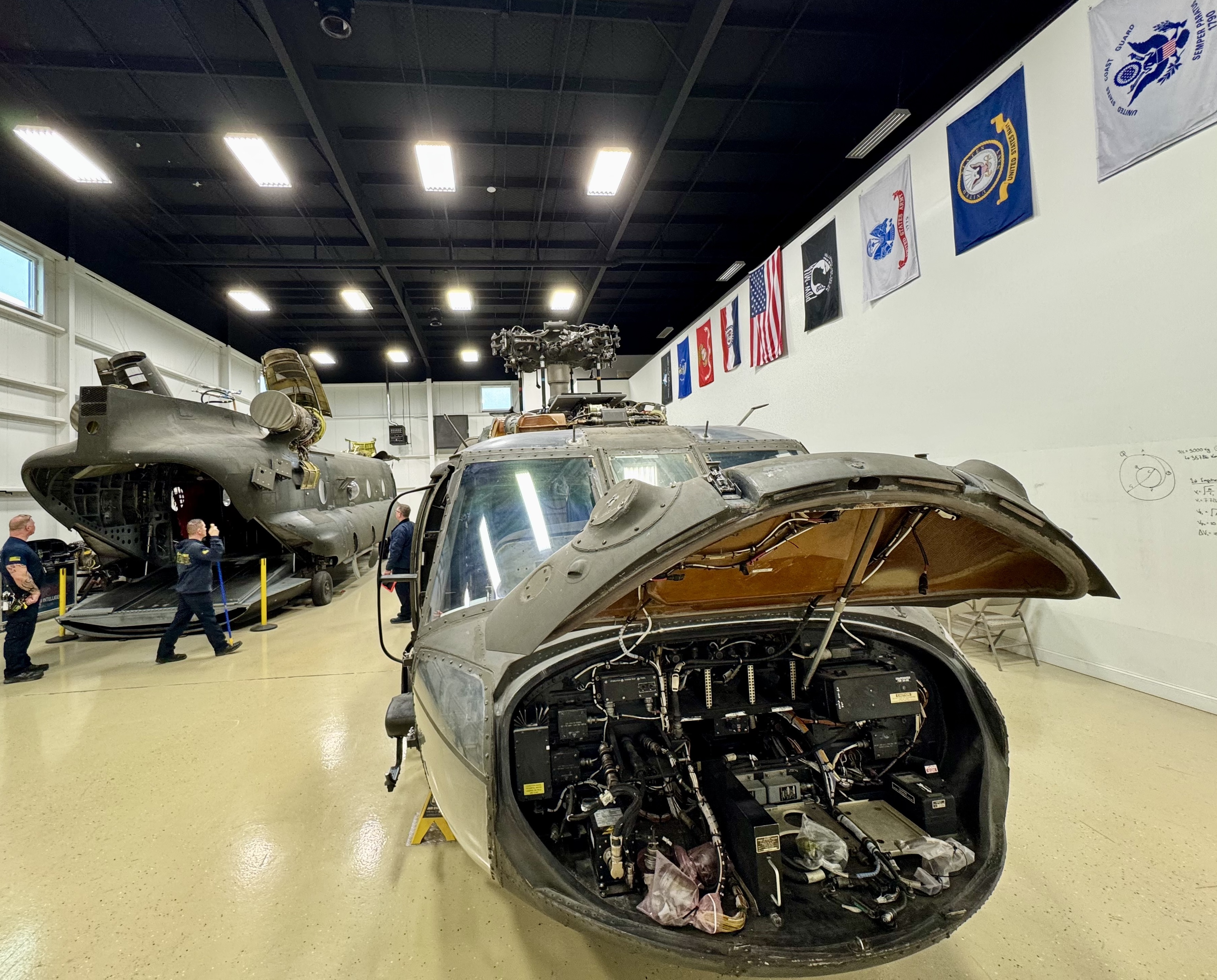 Open aircraft nose and helicopters inside a maintenance hangar.