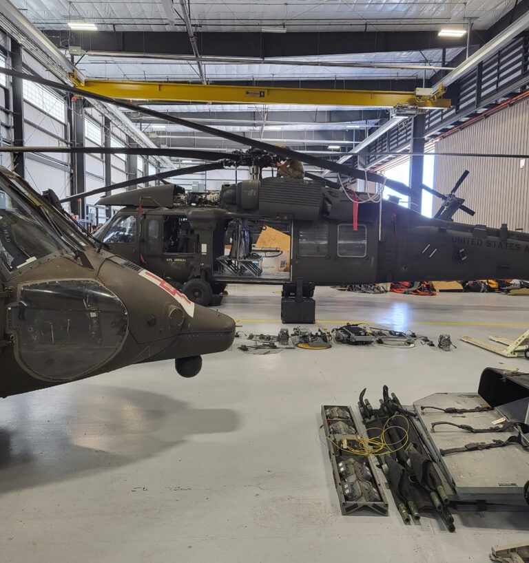 Helicopters inside a maintenance hangar with sustainment activity underway.